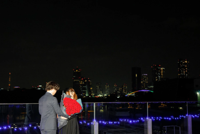 夜景を背景にバラの花束を抱えるカップル