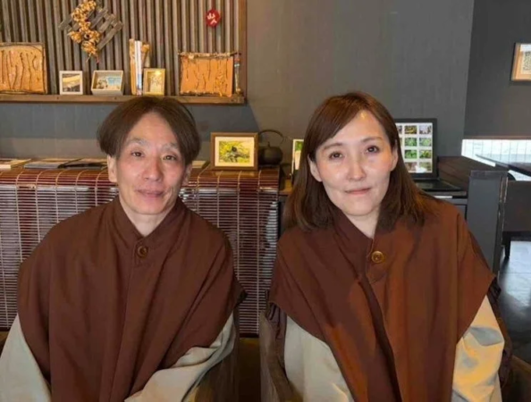 伝統的な雰囲気の場所で、茶色い衣装を着た男女が並んで座って微笑んでいます。