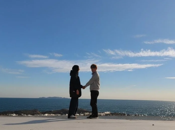 青い空と広がる海を背景に、二人の人物が手を取り合って向かい合っている写真です。