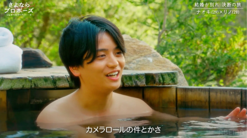 屋外の露天風呂に浸かり、笑顔を見せる若い男性の画像