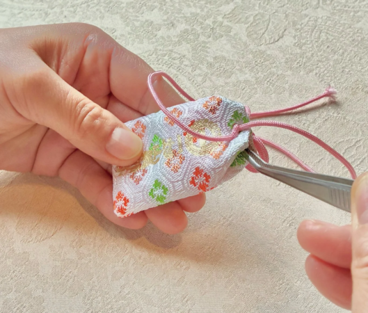 女性がお守り袋をピンセットで調整している画像