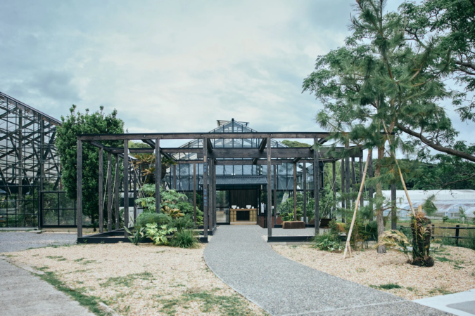 砂利道が続く先に、現代的なデザインの温室または植物園の入り口が見えます。